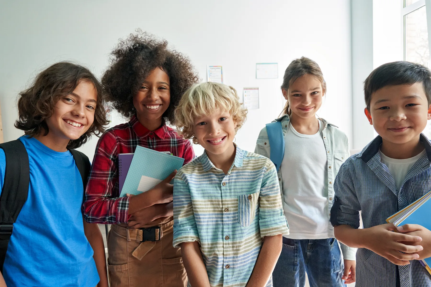 Five elementary and middle school students standing together in a bright classroom.